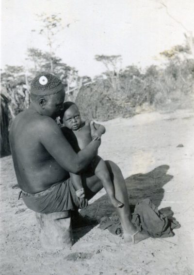 Soba Tchiliwandele holding a small child. He sold his hat to the Powell-Cottons but not the conus shell adorning it. The Powell-Cottons had to find an alternative conus for their collection.